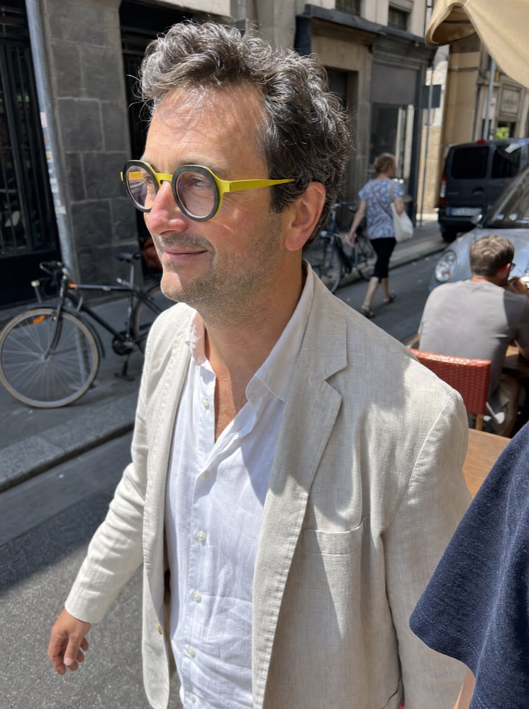 Un homme porte des lunettes à monture jaune dans une rue animée, image générée par IA